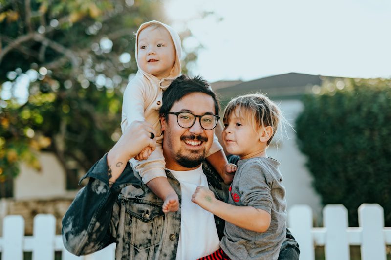 Father holding his two young children outside their home